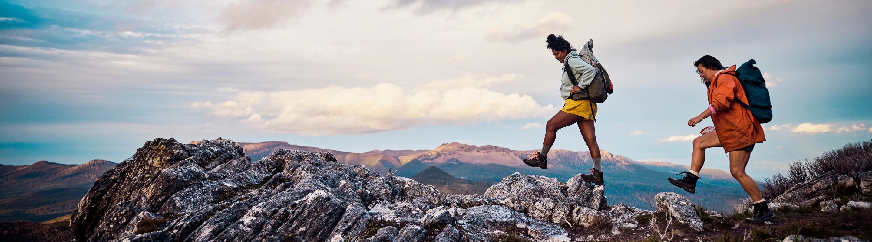two female bushwalkers cross a rocky mountain trail, insured with travel insurance for Australia