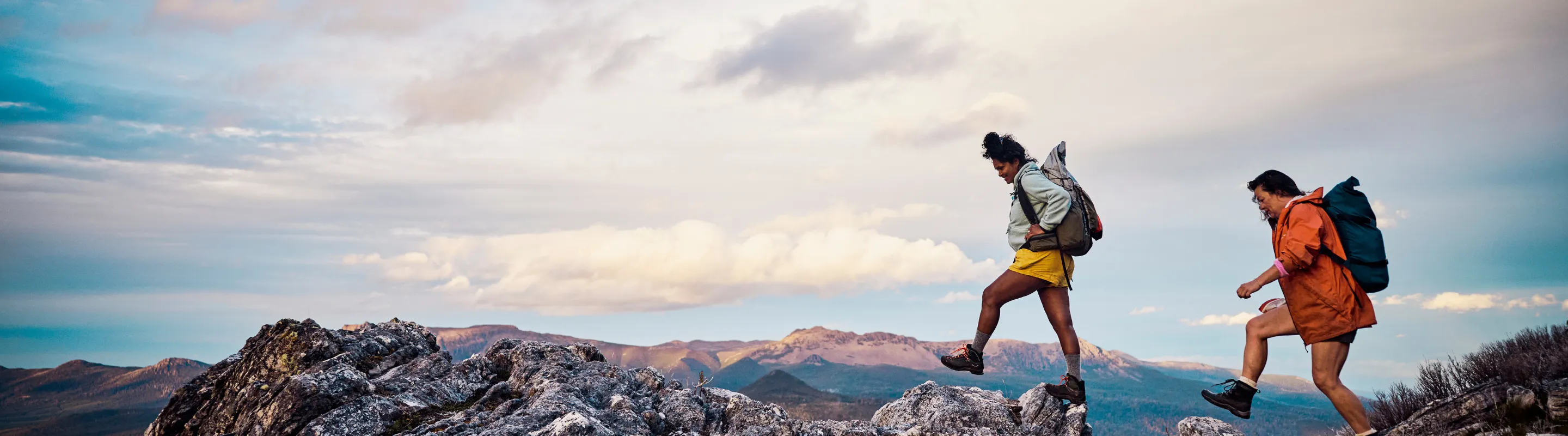 two female bushwalkers cross a rocky mountain trail, insured with travel insurance for Australia
