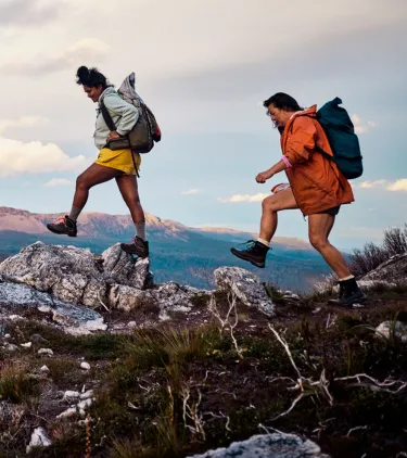two female bushwalkers cross a rocky mountain trail, insured with travel insurance for Australia