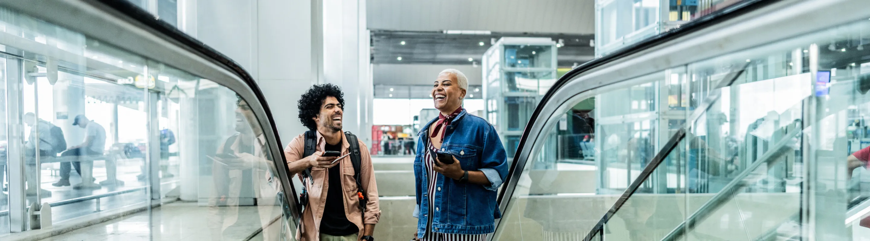 a man and woman with accidental death travel insurance, laughing as they take an escalator at an airport 
