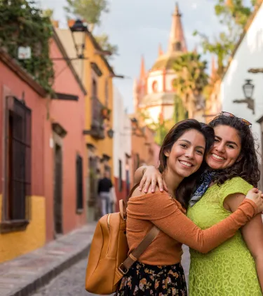 two women with travel insurance for Mexico hug and pose in front of San Miguel de Allende 