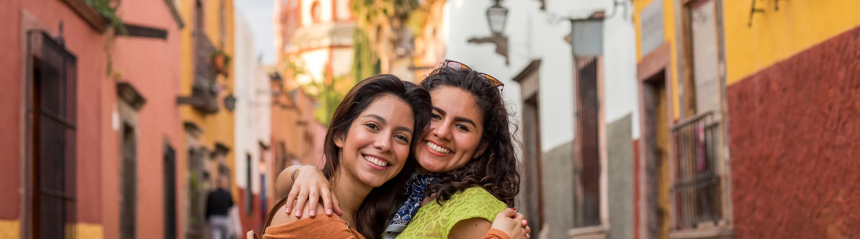 two women with travel insurance for Mexico hug and pose in front of San Miguel de Allende 