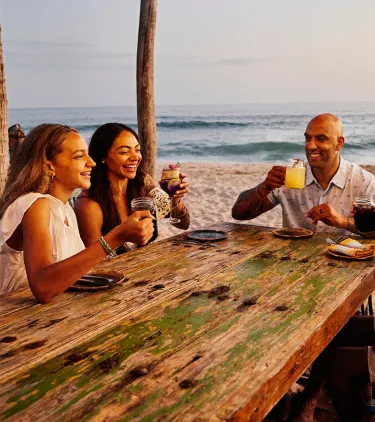 four friends dine on a beach at a resort, insured with travel insurance for Mexico
