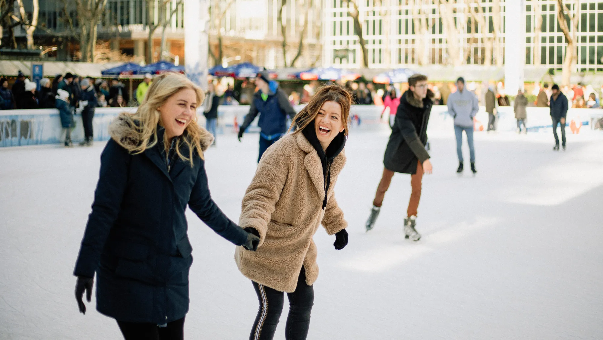 friends hold hands as they ice skate in New York City on vacation, wondering "Does travel insurance cover snowstorms?"