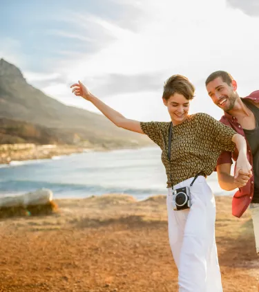 two friends laugh and explore a coastal trail at sunset in Cape Town, insured with travel insurance for Africa 
