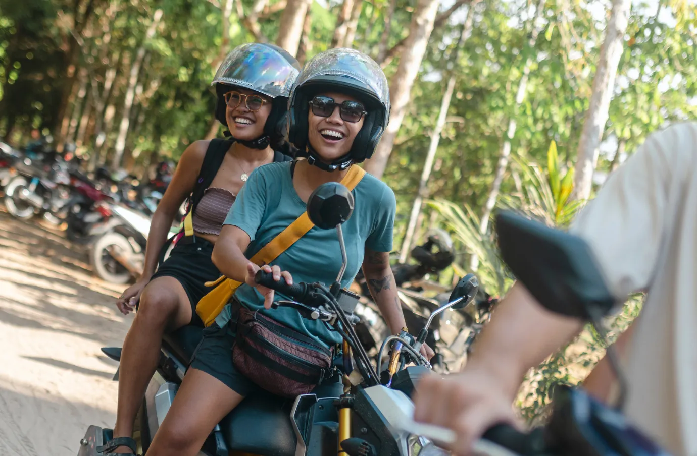 two women with travel insurance for the Philippines ride a scooter along a tropical road lined with trees