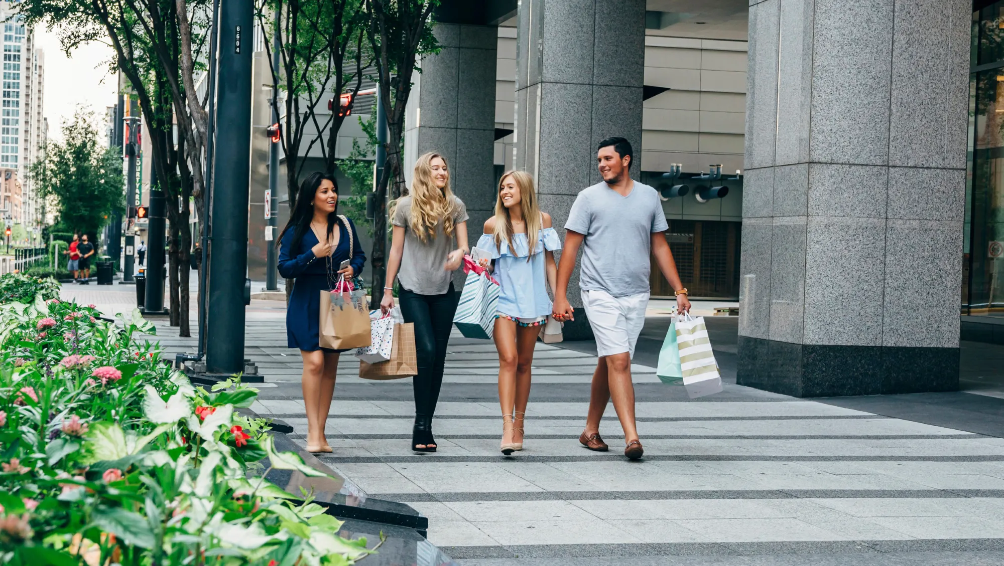 friends walk through downtown Dallas with shopping bags on vacation after asking, "How much is travel insurance?"