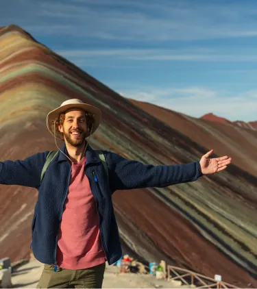 a young man stands and raises his arms at Rainbow Mountain, Peru, insured with travel insurance for South America 