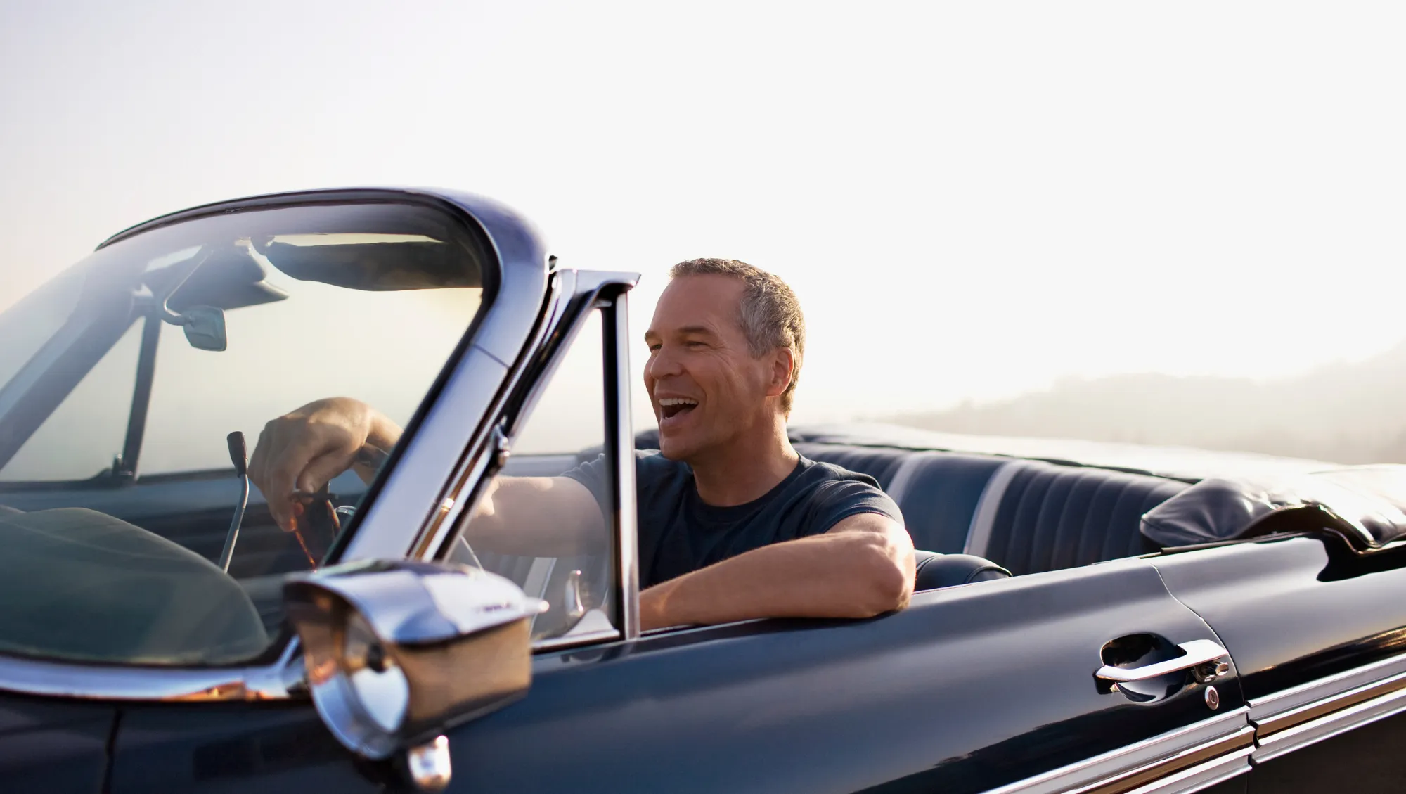 a middle-aged man drives a convertible by a coast, knowing what to do if he gets in a vehicle accident on vacation