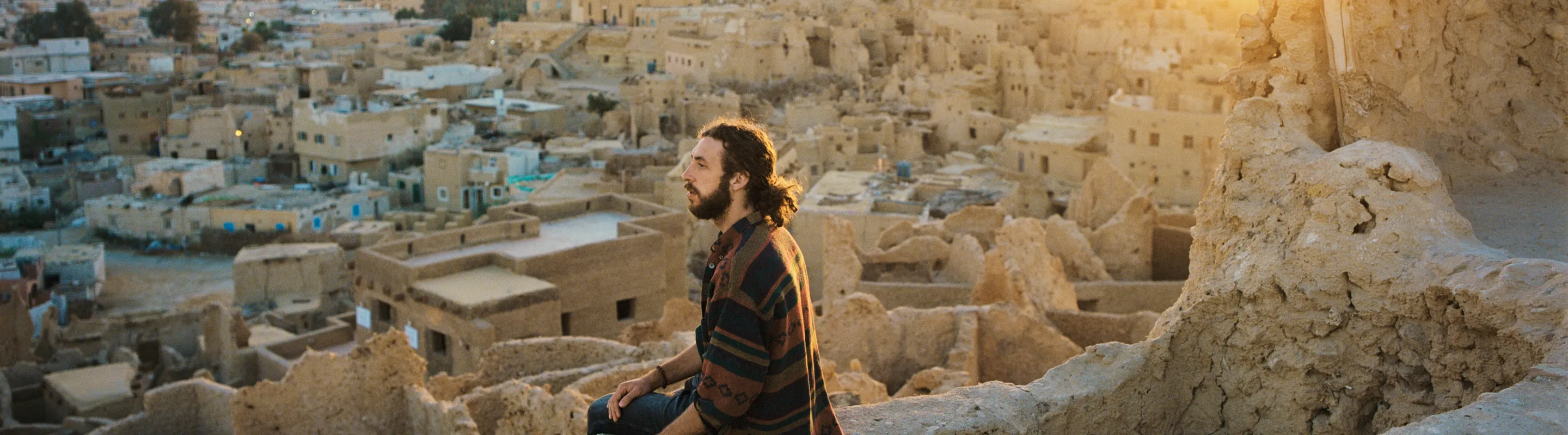a young man sits on a ledge and overlooks the Siwa Oasis at sunset, insured with travel insurance for Egypt