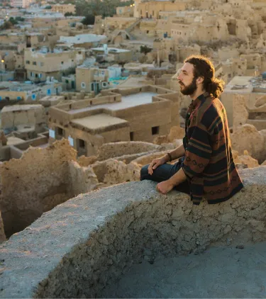 a young man sits on a ledge and overlooks the Siwa Oasis at sunset, insured with travel insurance for Egypt