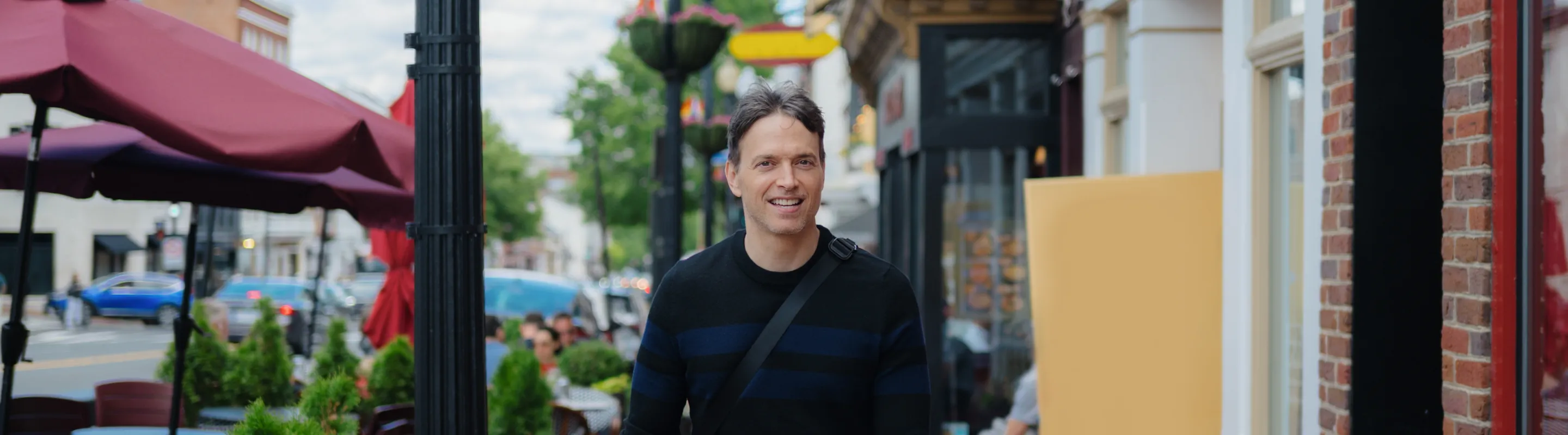 a man with travel insurance for Washington, D.C. walks along a brick sidewalk lined with restaurants, shops, and outdoor seating