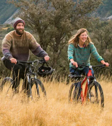 a man and woman biking through Hooker Valley in autumn with travel insurance for New Zealand
