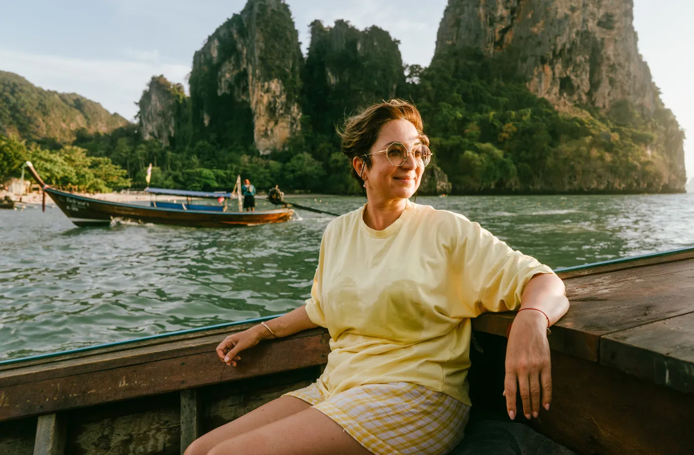 a mature woman with solo travel insurance sits in a wooden boat on a river with limestone cliffs 