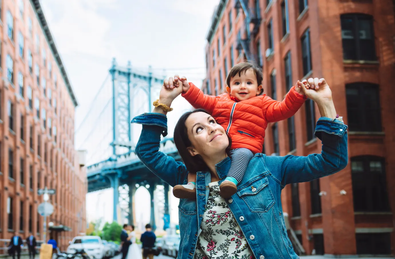 a mother with travel insurance for New York carries her toddler son on her shoulders in Brooklyn