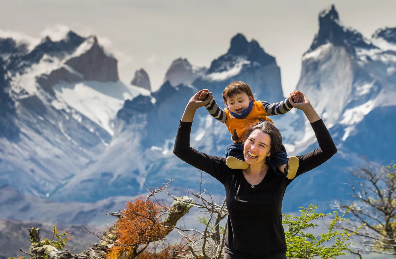 a mother holds her toddler son on her shoulders in the Patagonia mountains, insured with travel insurance for South America  