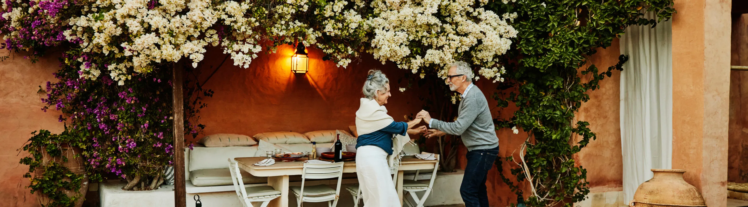 a senior couple with travel delay insurance dances on an outdoor patio in the Mediterranean under flowering vines