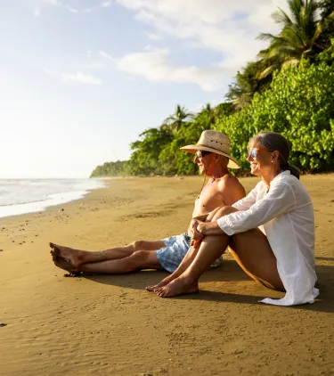 a senior couple sits and relaxes on a tropical beach, insured with travel insurance for Costa Rica