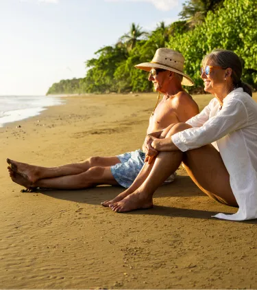 a senior couple sits and relaxes on a tropical beach, insured with travel insurance for Costa Rica
