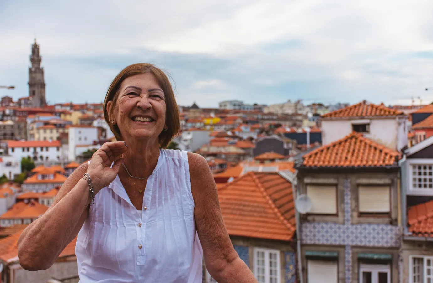 a senior woman stands and smiles on an overlook of Porto, Portugal, insured with travel insurance for Portugal