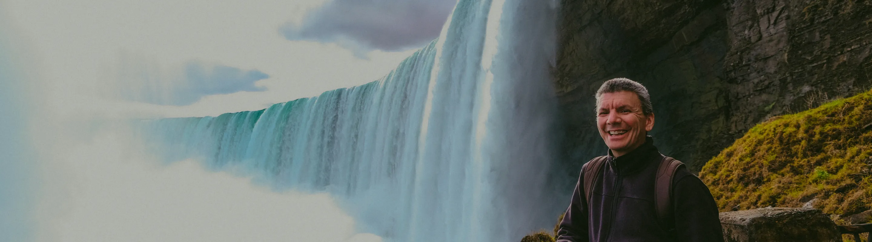 a male tourist smiles on a lookout point at Niagara Falls, insured with travel insurance for Canada
