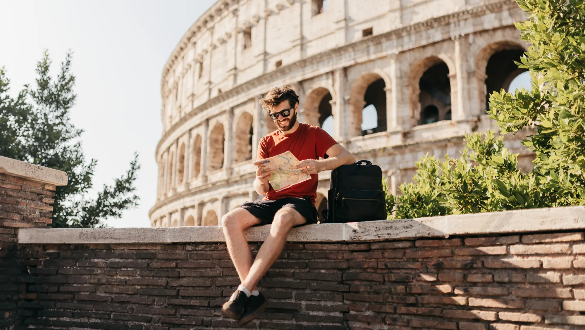 a man with a backpack looks at a map near the Colosseum in Rome, hoping to prevent theft on vacation 