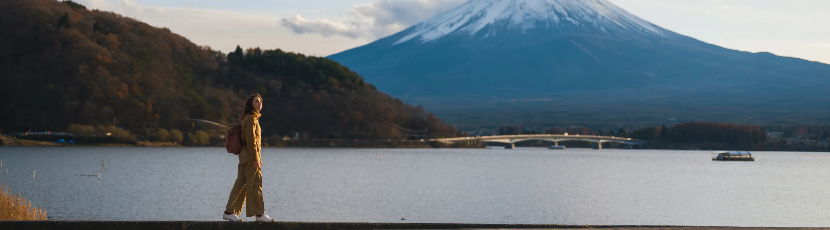 a female solo traveler in a yellow jacket walks near Mount Fuji, insured with travel insurance for Japan