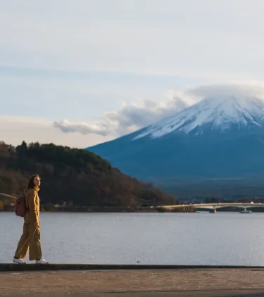 a female solo traveler in a yellow jacket walks near Mount Fuji, insured with travel insurance for Japan