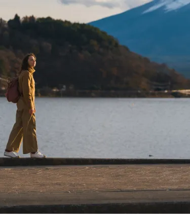 a female solo traveler in a yellow jacket walks near Mount Fuji, insured with travel insurance for Japan