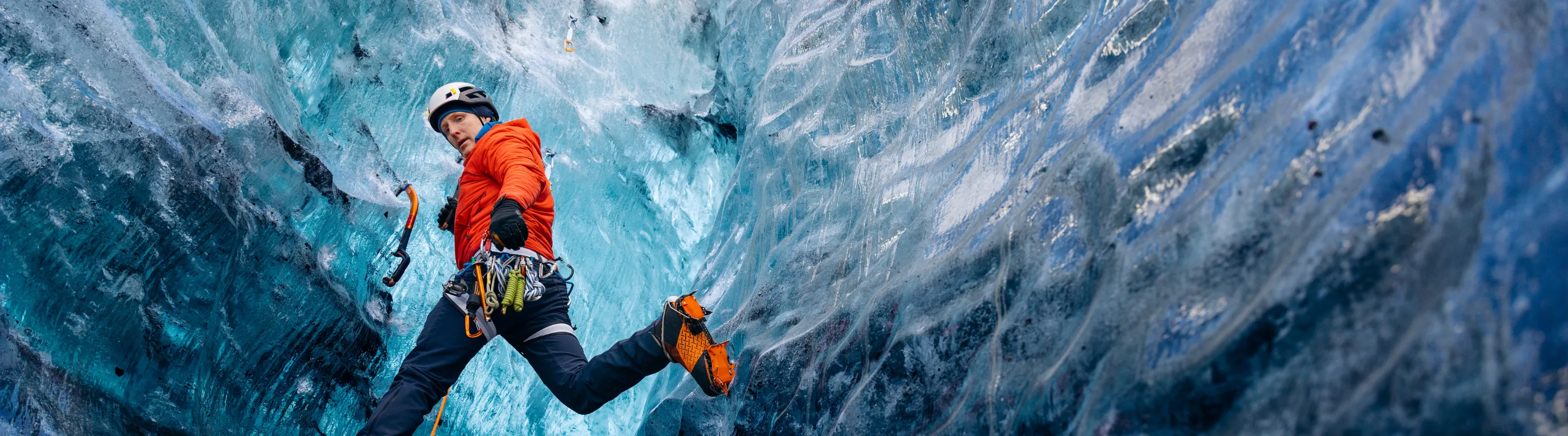 a young man in a red jacket climbs a glacier in safety gear, insured with travel insurance for Iceland 
