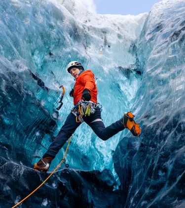 a young man in a red jacket climbs a glacier in safety gear, insured with travel insurance for Iceland 
