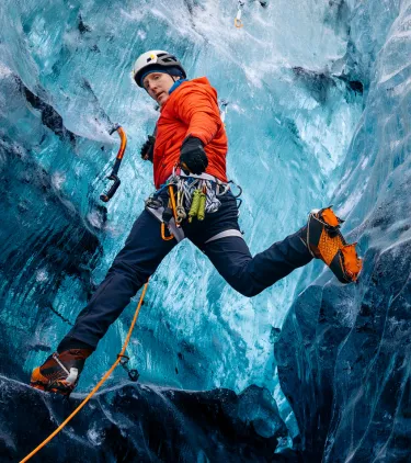a young man in a red jacket climbs a glacier in safety gear, insured with travel insurance for Iceland 