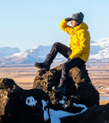 a man in a yellow jacket overlooks a black sand beach, insured with travel insurance for Iceland 