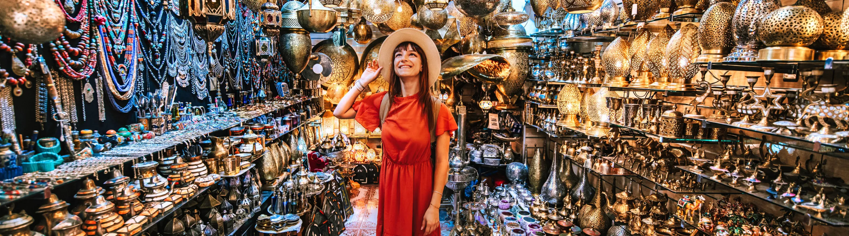 a young woman in a red dress looks around in a Moroccan lanterns market, insured with travel insurance for Morocco