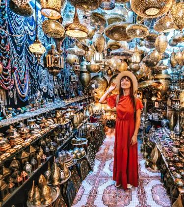 a young woman in a red dress looks around in a Moroccan lanterns market, insured with travel insurance for Morocco