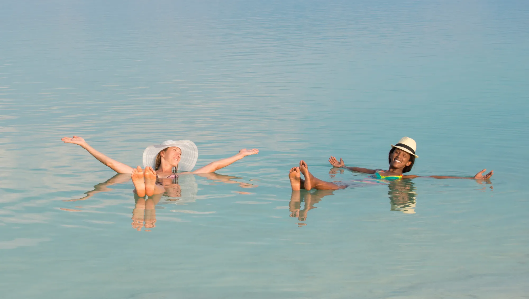 two women float in the Dead Sea in Jordan after asking, "How much is travel insurance?" and buying coverage 