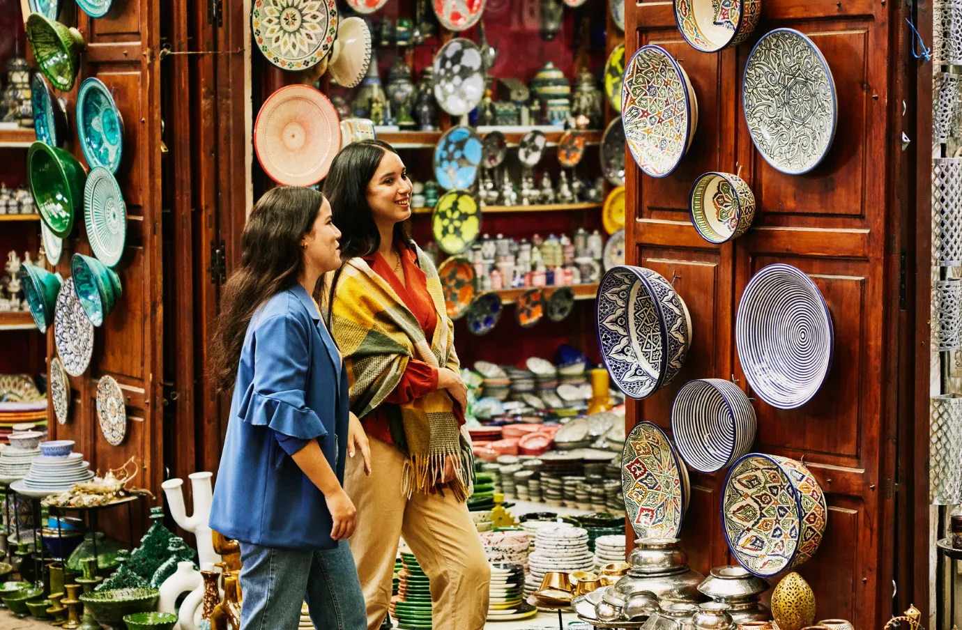 two females shop for ceramics in a Moroccan market, insured with travel insurance for Morocco