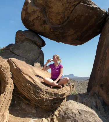 a young woman sits and drinks water in Big Bend National Park, insured with travel insurance for Texas