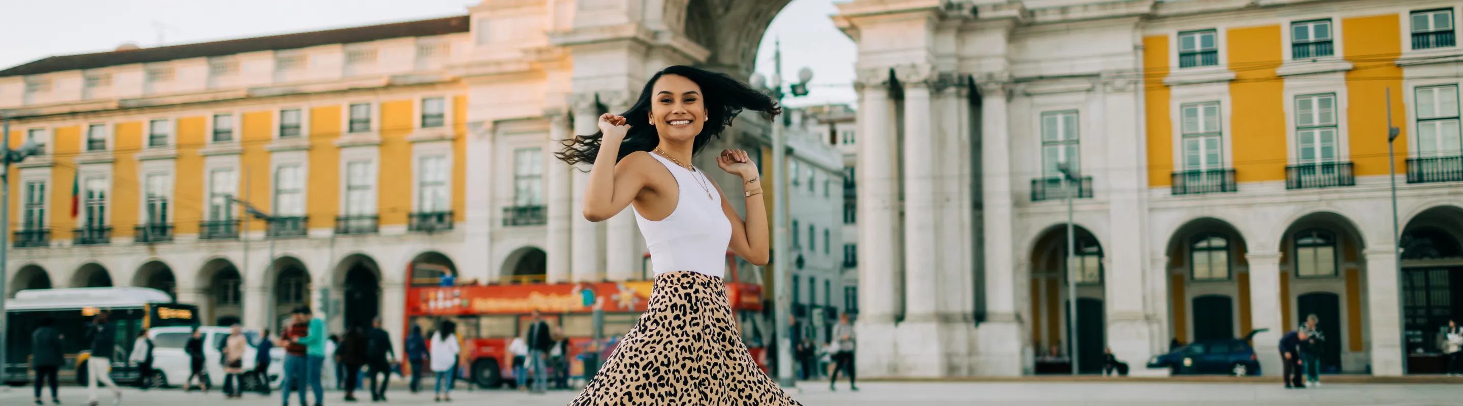 a young woman spins in Commerce Square, Lisbon, insured with travel insurance for Portugal