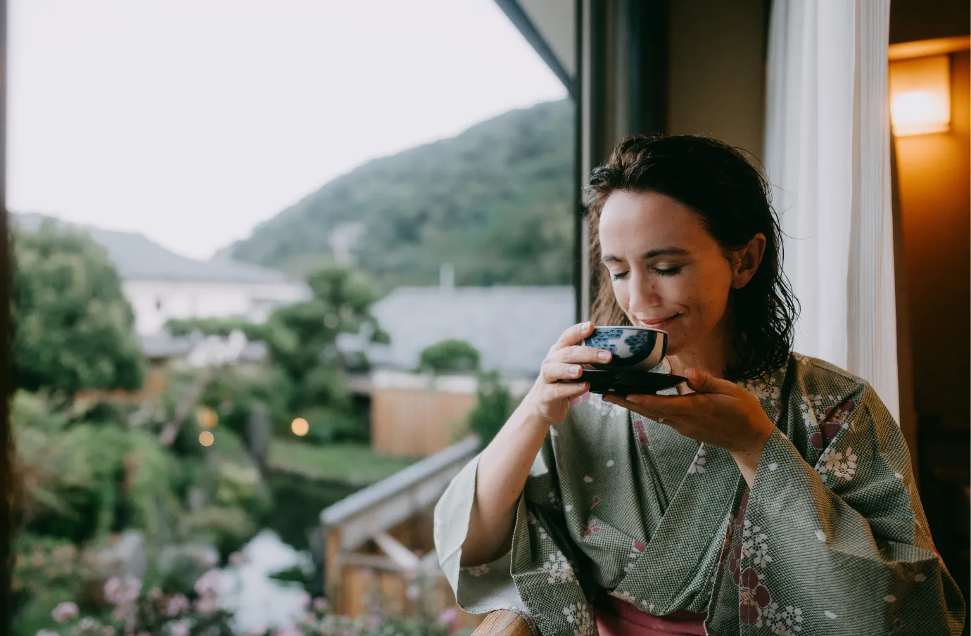 a middle-aged woman drinks tea in a Japanese Ryokan near a window, insured with travel insurance for Japan