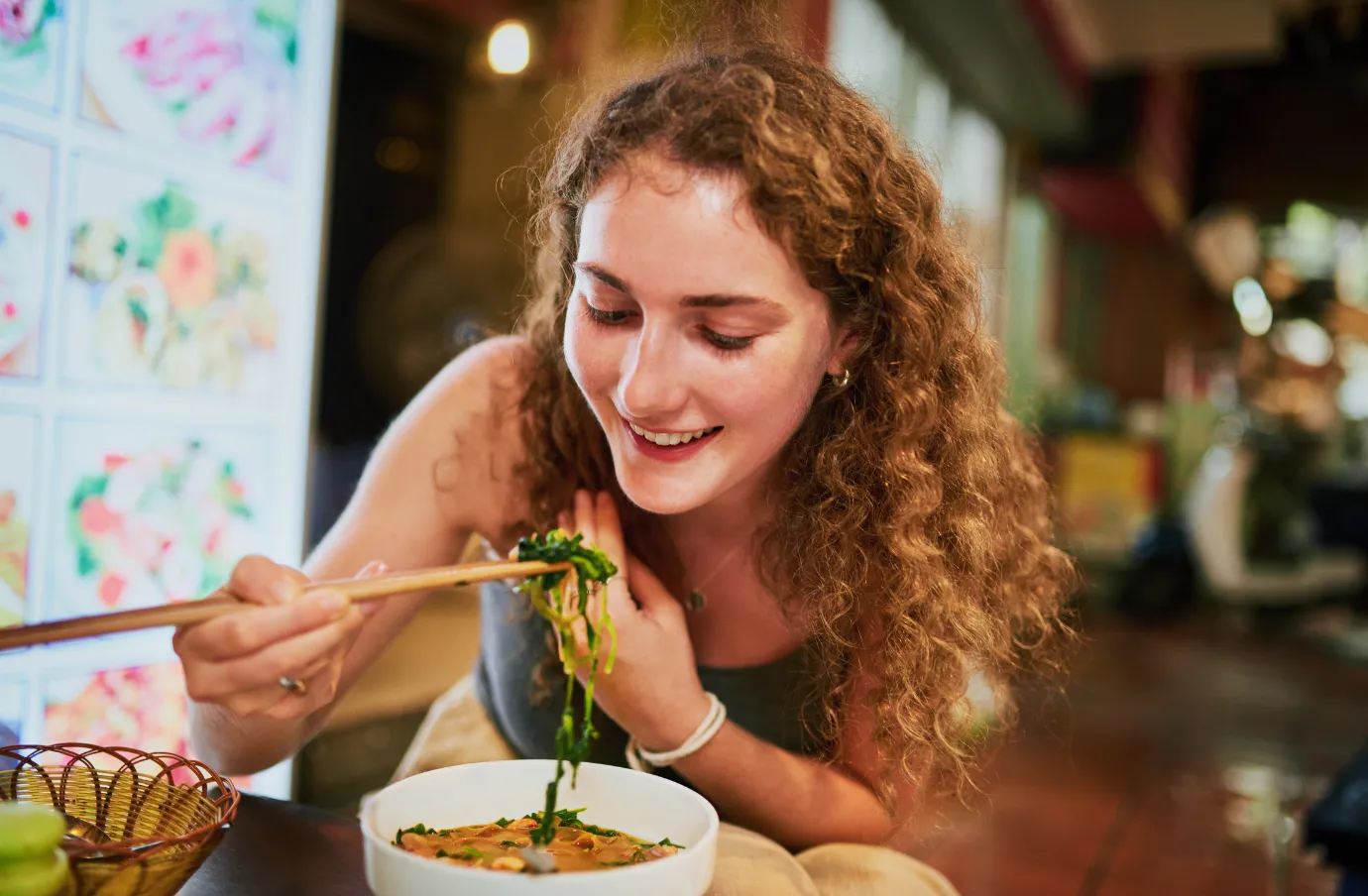 a woman with travel insurance for Vietnam uses chopsticks to eat a traditional pho at a local restaurant