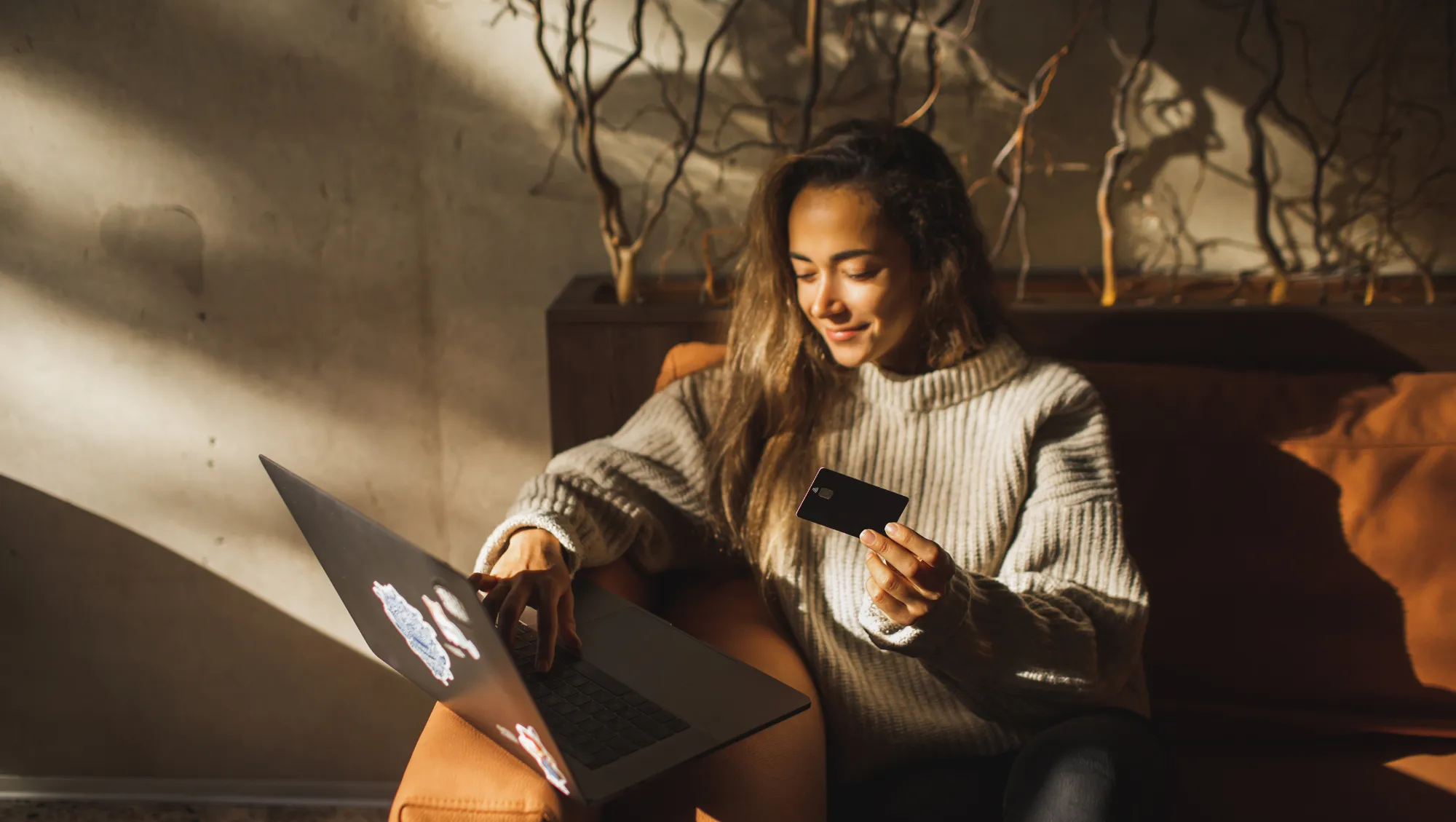 a woman sits on a couch with natural light, holding her credit hard and looking up "How much is travel insurance?"