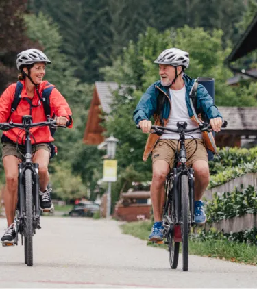 a man and woman with travel insurance for Austria, biking through a small Austrian town in the country