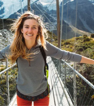 a young woman with travel insurance for New Zealand crosses a mountain suspension bridge 