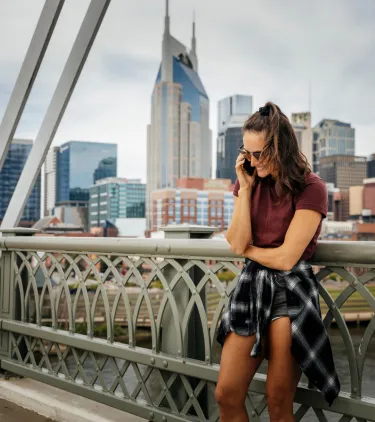 a woman stands talks on the phone on a bridge near the Nashville skyline, insured with travel insurance for Tennessee