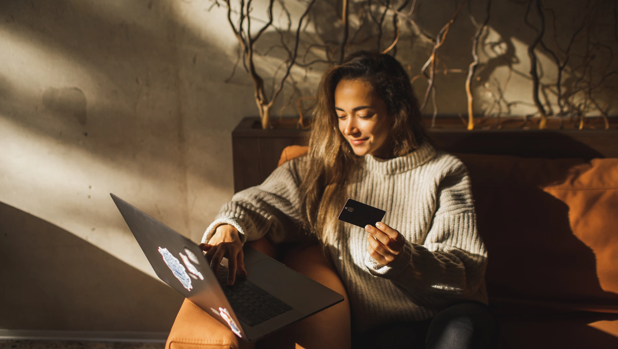 a woman looks at her laptop and holds her credit card, looking up the pros and cons of credit card travel insurance 