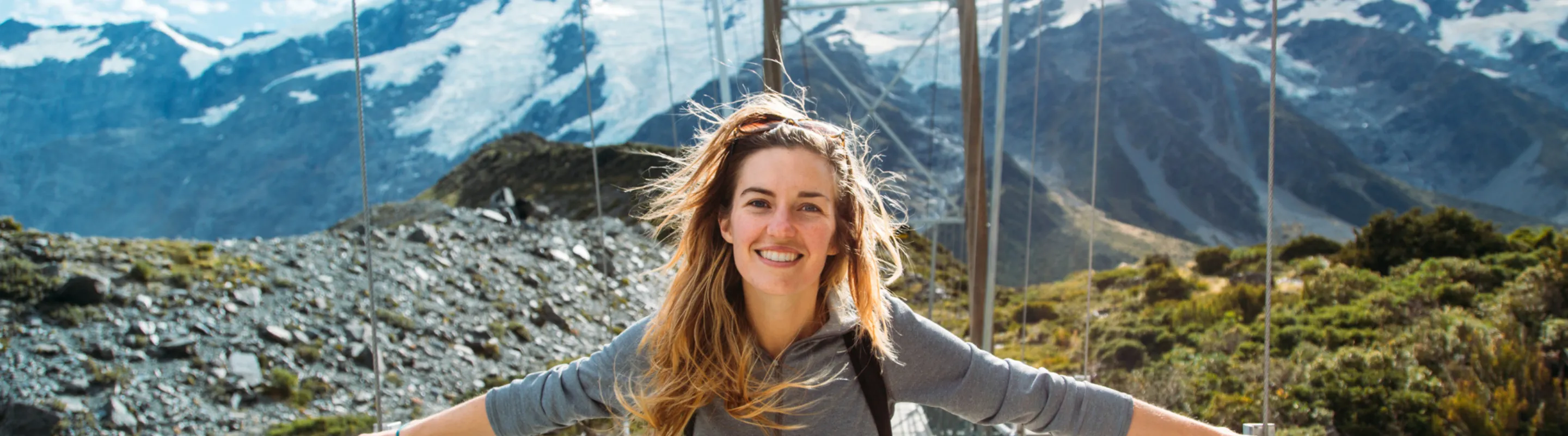 a young woman with travel insurance for New Zealand crosses a mountain suspension bridge 