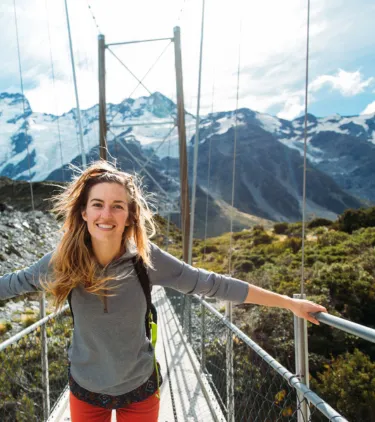 a young woman with travel insurance for New Zealand crosses a mountain suspension bridge 