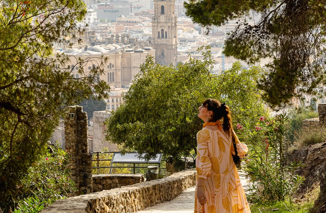 a woman walks down a scenic path overlooking the city of Malaga, insured with travel insurance for Spain