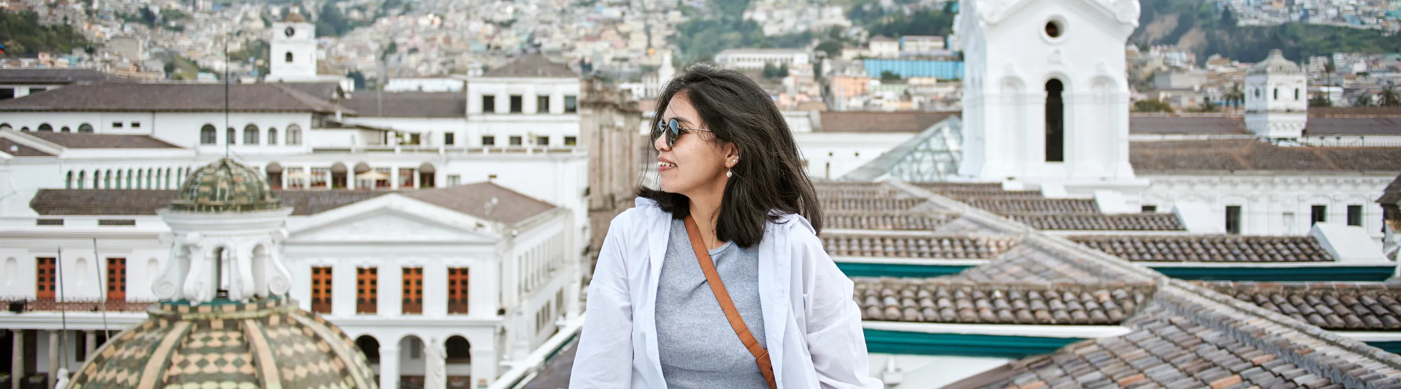 a young woman sits on a ledge overlooking Quito, Ecuador, insured with travel insurance for South America 